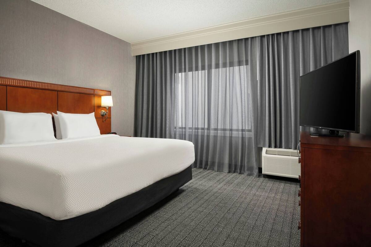 A hotel room with a bed, a television, a desk, and a window with curtains.