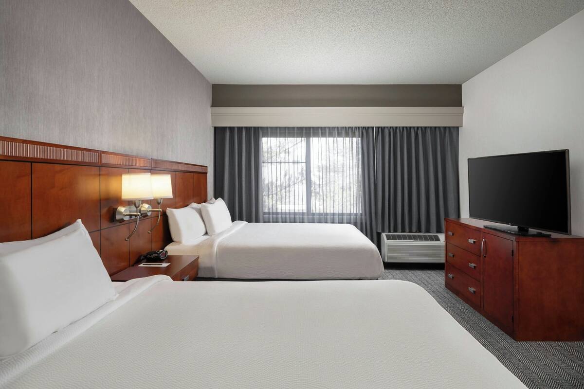 A hotel room with two beds, a TV, a desk with a lamp, and a window with curtains.