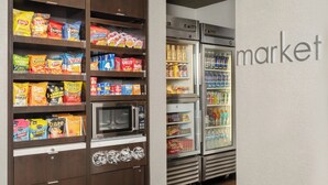 A snack and beverage display in a market setting with a microwave and refrigerators.