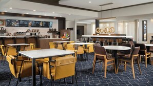 A hotel dining area with tables and chairs, a bar, and a menu display.