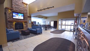 A hotel lobby with a stone fireplace, blue sofas, a flat-screen TV, and a dining area with tables and chairs. - Best Western Resort Hotel & Conference Center (Portage)
