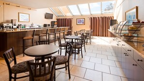 A modern dining area with round tables and chairs, a kitchen counter with appliances, and a large window providing natural light. - Best Western Resort Hotel & Conference Center (Portage)