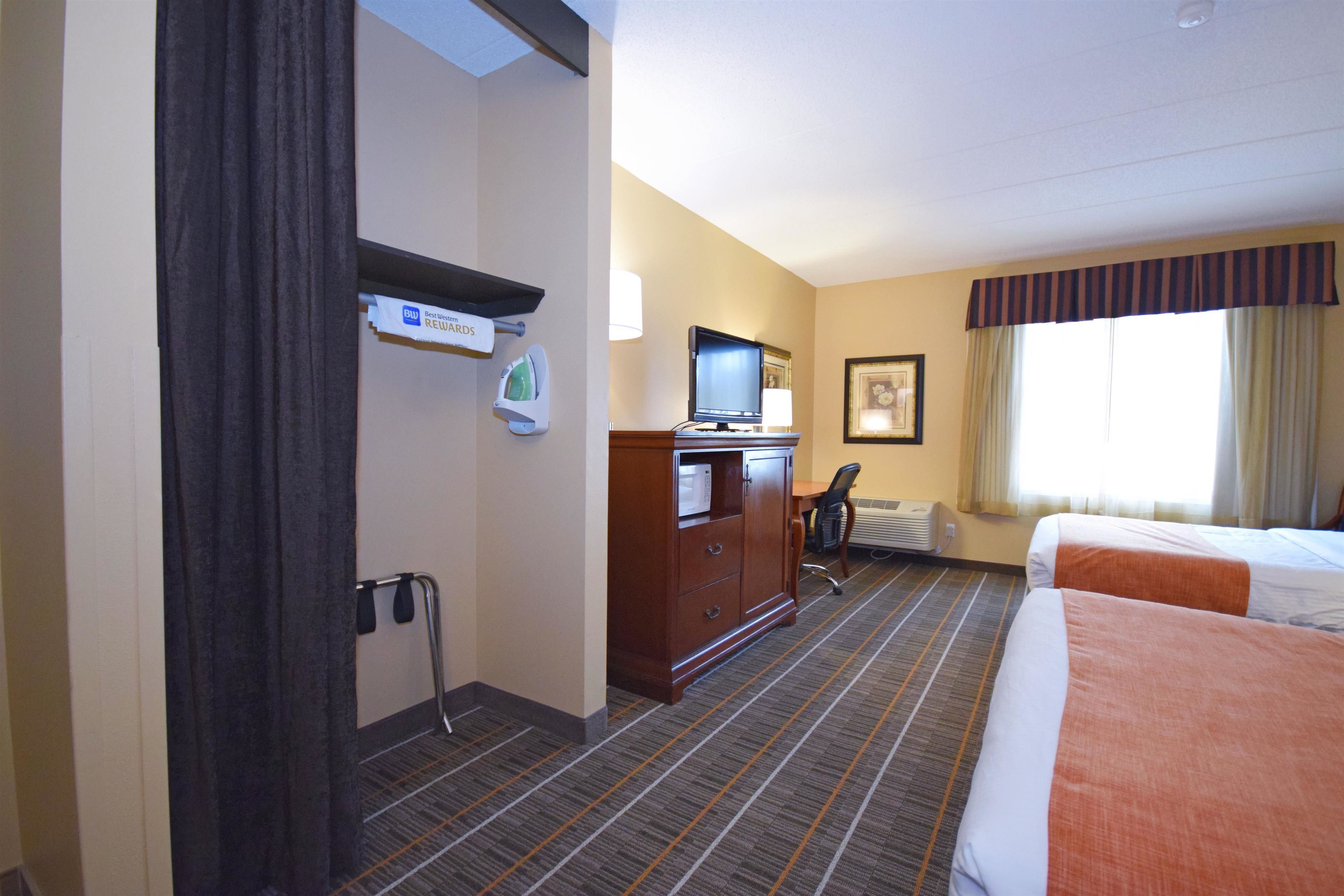 Une chambre d’hôtel avec deux lits, un bureau avec un ordinateur, une télévision et une fenêtre avec des rideaux.