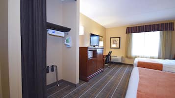 Une chambre d’hôtel avec deux lits, un bureau avec un ordinateur, une télévision et une fenêtre avec des rideaux.