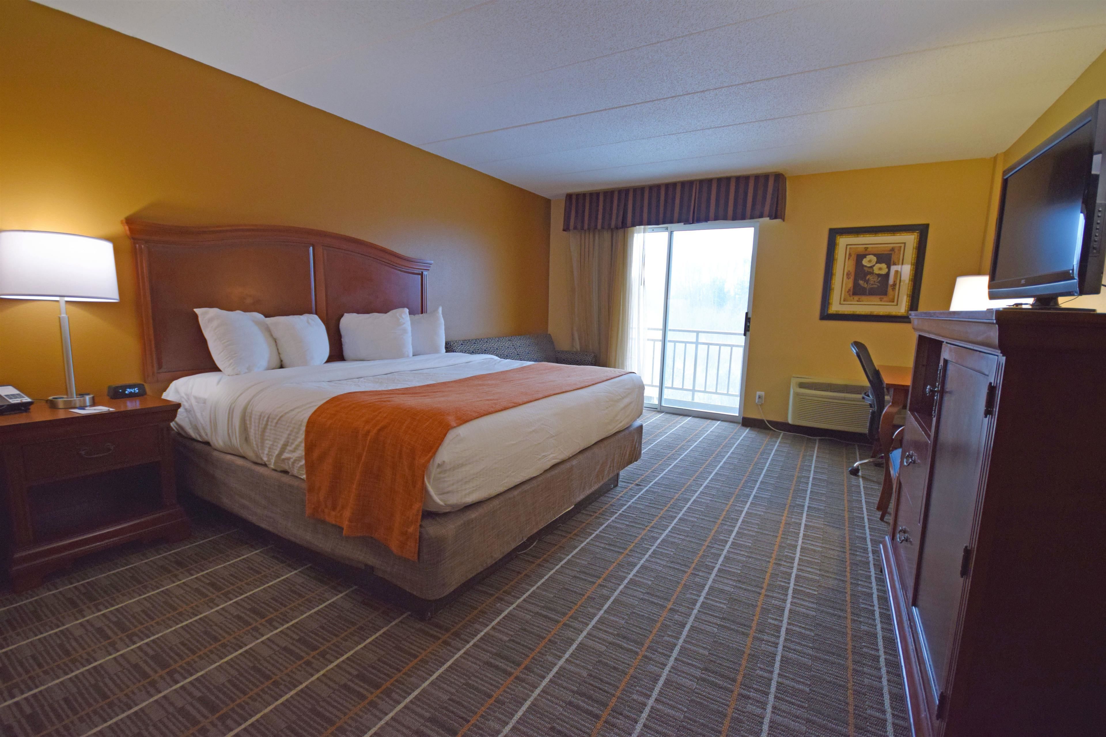 A hotel room with a large bed, a desk with a lamp, a television, and a view of the outdoors.
