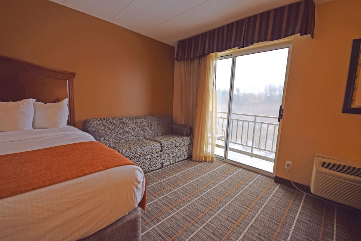 Ein Hotelzimmer mit einem großen Bett, einer Sitzecke, einem Balkon mit Vorhängen und einem Fenster.