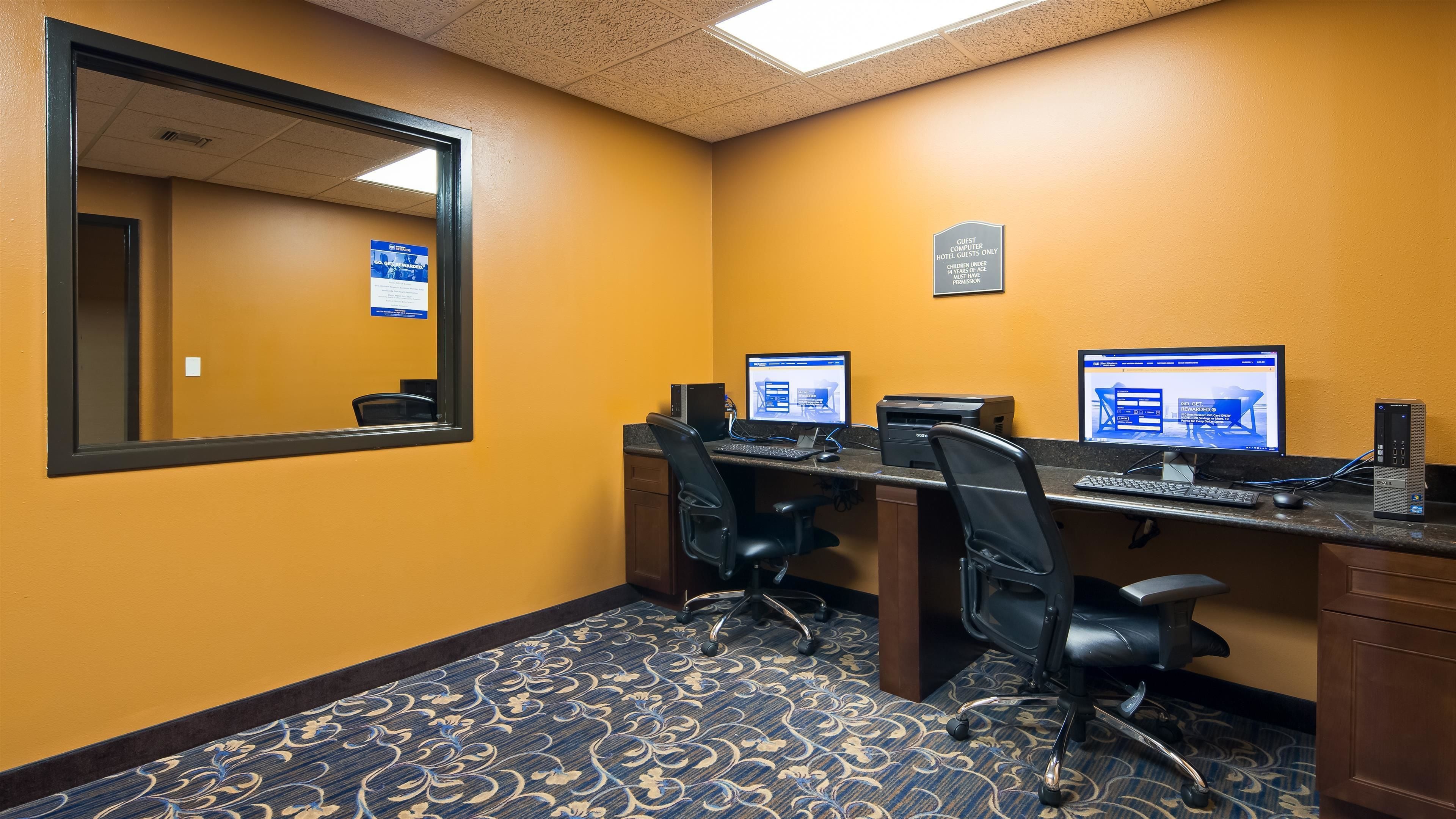 A hotel room with two computer workstations, a large mirror, and a carpeted floor.