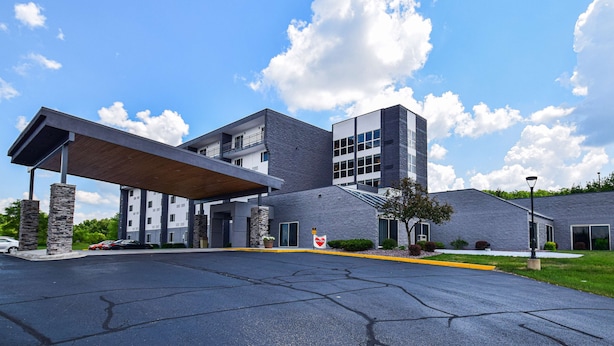 A modern building with a covered entrance, a parking lot, and a grassy area with a flagpole. - Best Western Resort Hotel & Conference Center (Portage)