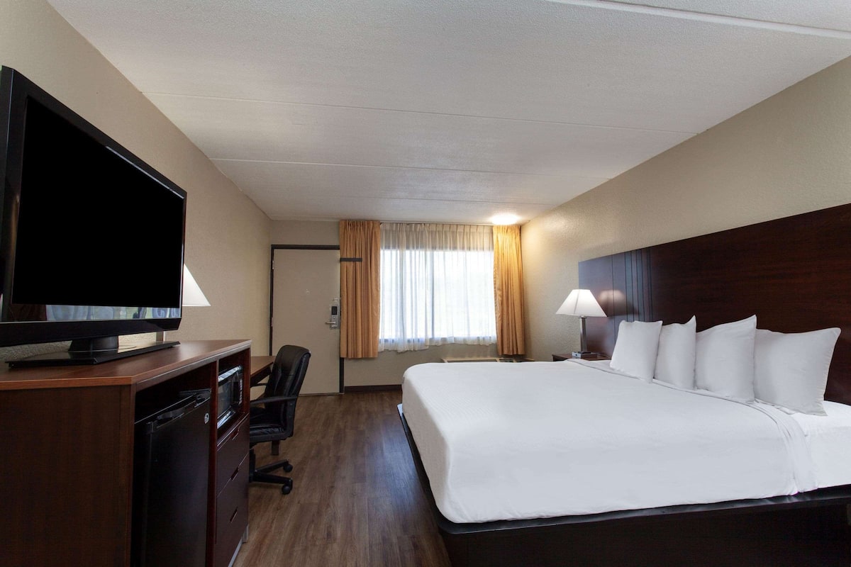Une chambre d’hôtel avec un grand lit, un téléviseur posé sur un meuble en bois, un bureau avec une chaise et une fenêtre avec des rideaux.