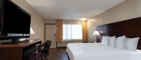 Habitación de hotel con una cama grande, un televisor sobre un mueble de madera, un escritorio con una silla y una ventana con cortinas.