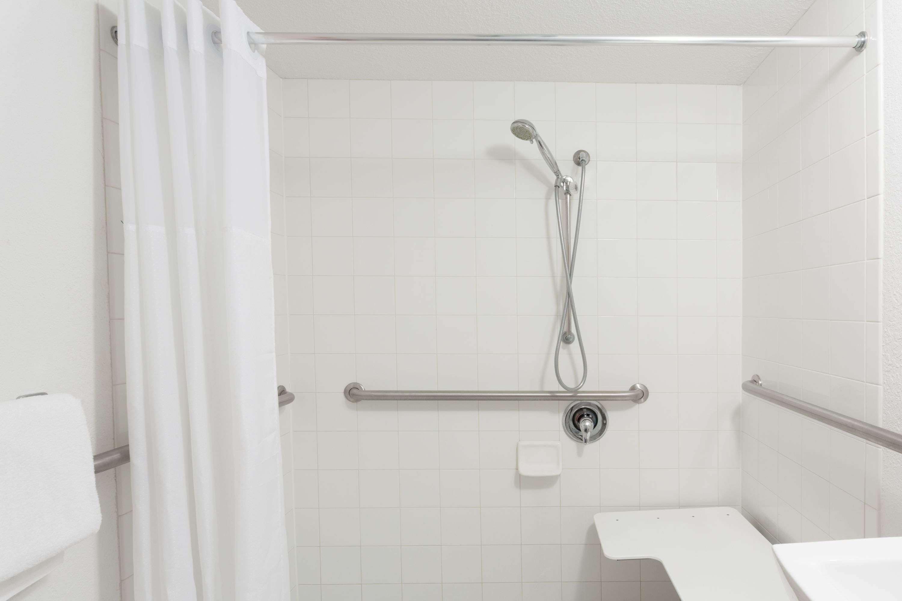 A bathroom with a shower, grab bar, and a white sink.