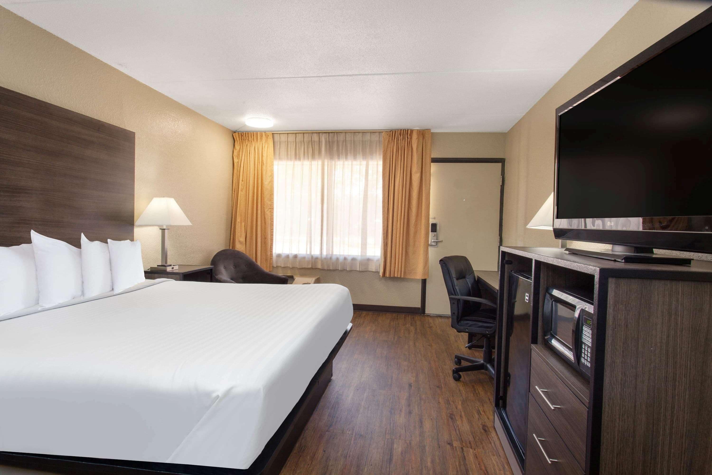 A hotel room with a large bed, a desk with a lamp, a television, and a microwave.