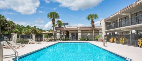 A swimming pool with lounge chairs and a building with balconies.