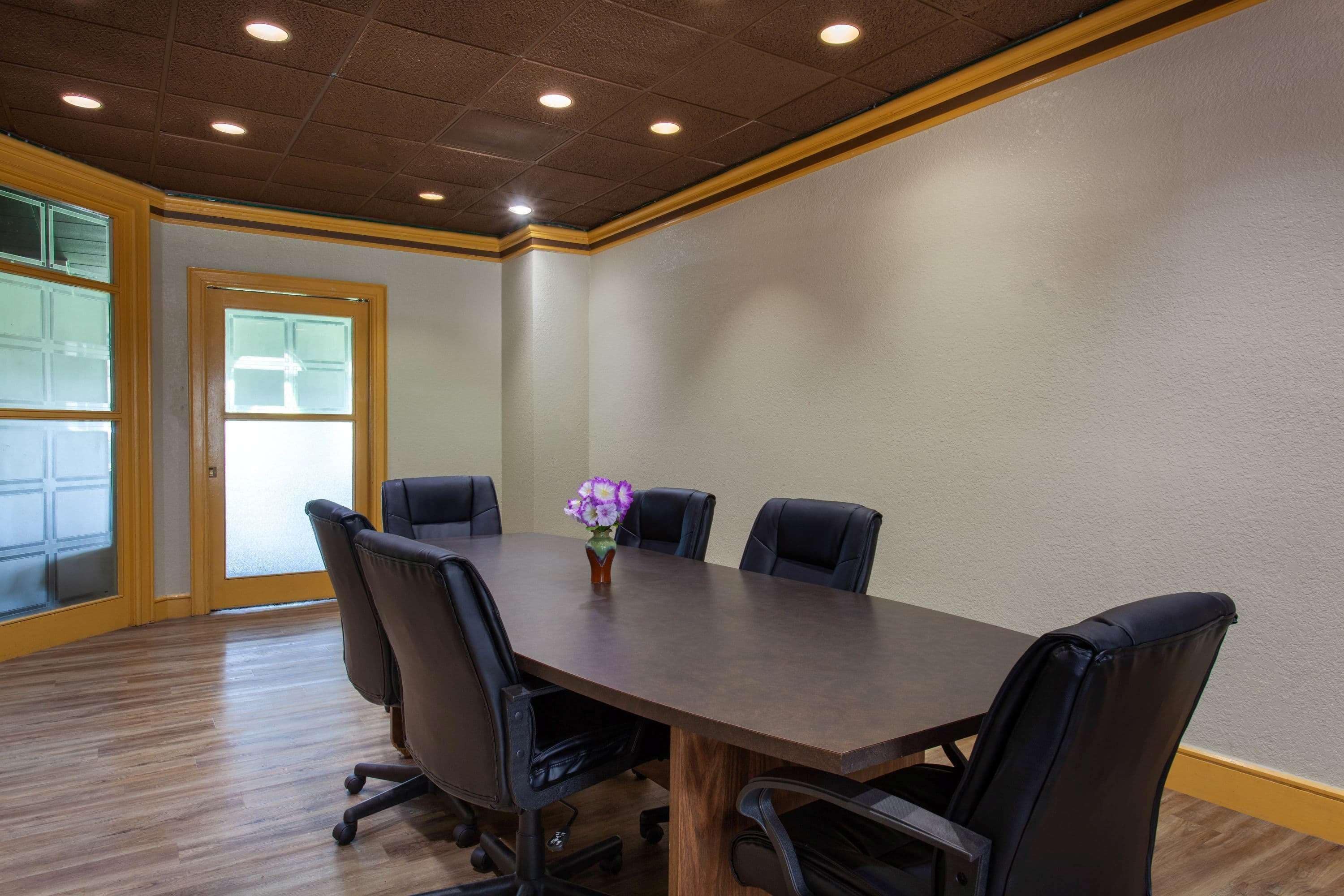 A conference room with a wooden table, six black chairs, and a vase with purple flowers.