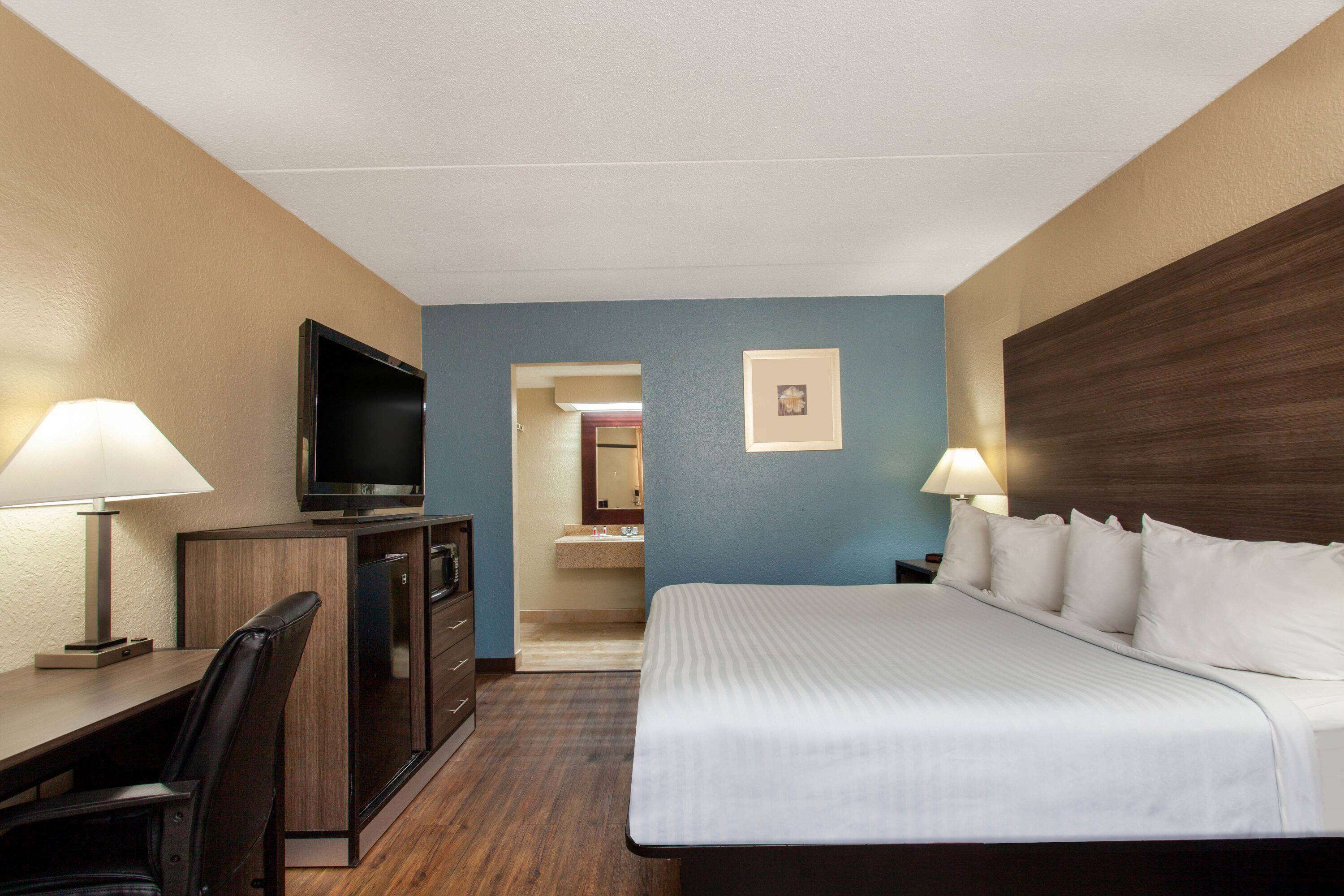 A hotel room with a bed, desk, chair, TV, and a bathroom visible through an open door.