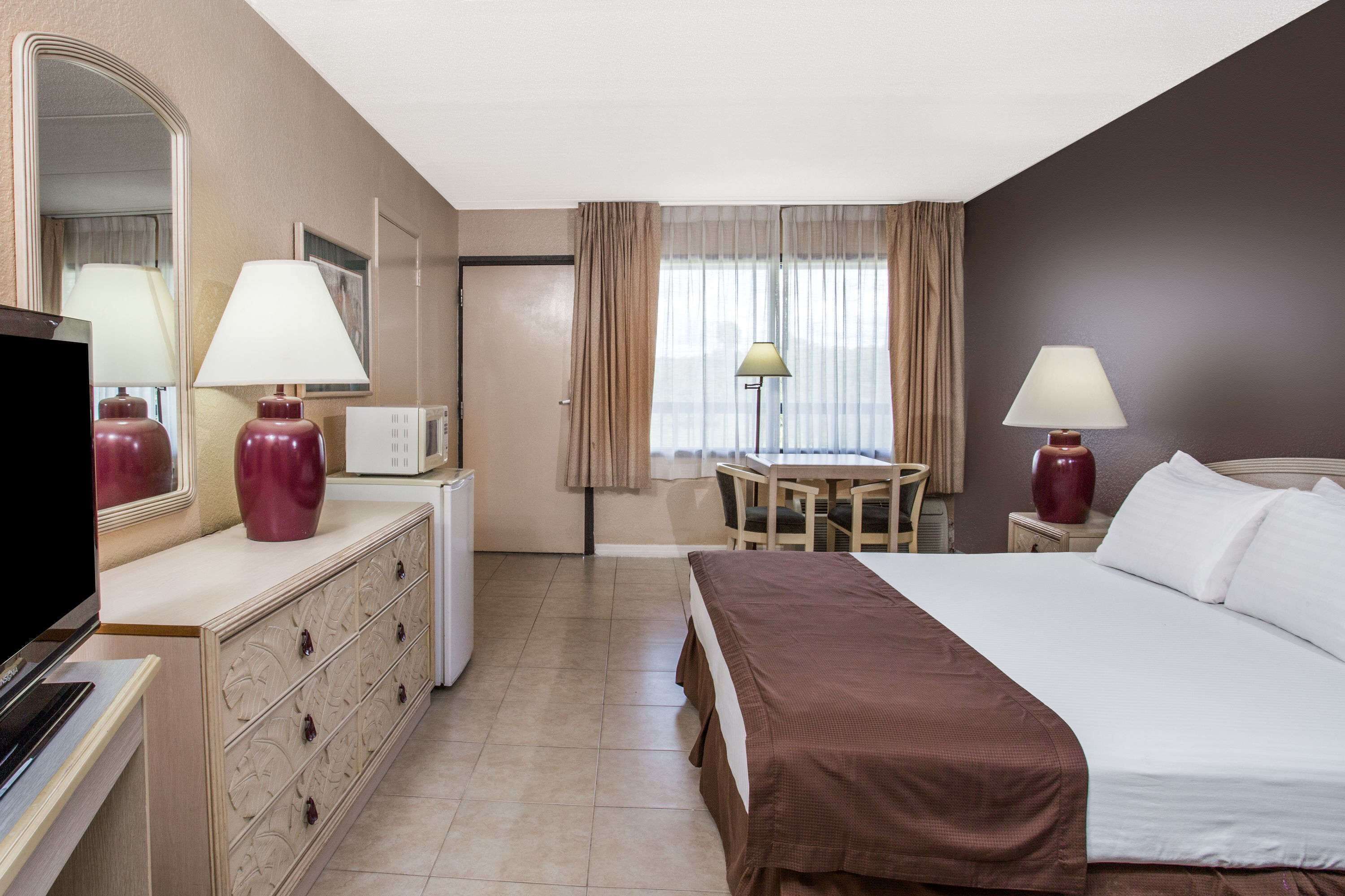 A hotel room with a bed, a desk, a chair, a television, a dresser, and a window with curtains.