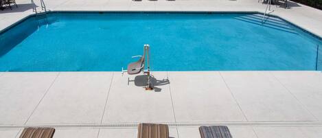 A swimming pool with lounge chairs and sun loungers around it, a lifeguard stand, and a fenced area with a bench and umbrella.