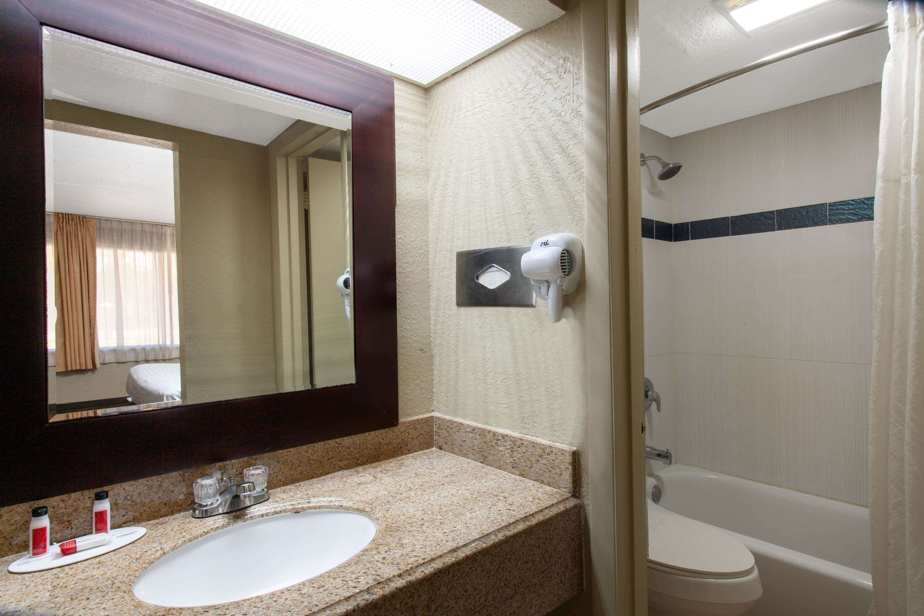Un baño con lavamanos, espejo, secador de pelo y ducha.