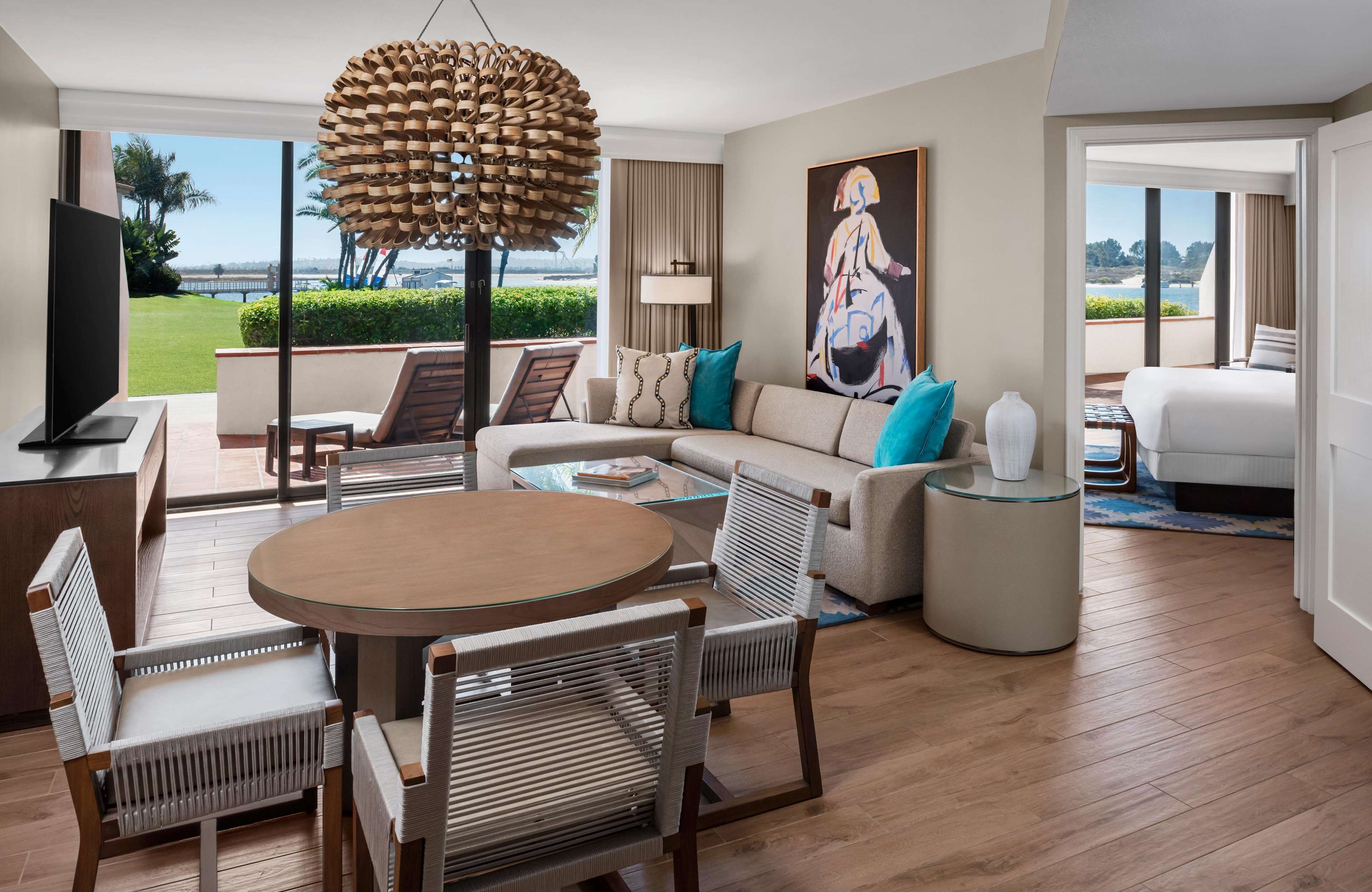 Una habitación de hotel moderna con un ventanal grande, una mesa de comedor redonda y un sofá con cojines decorativos.
