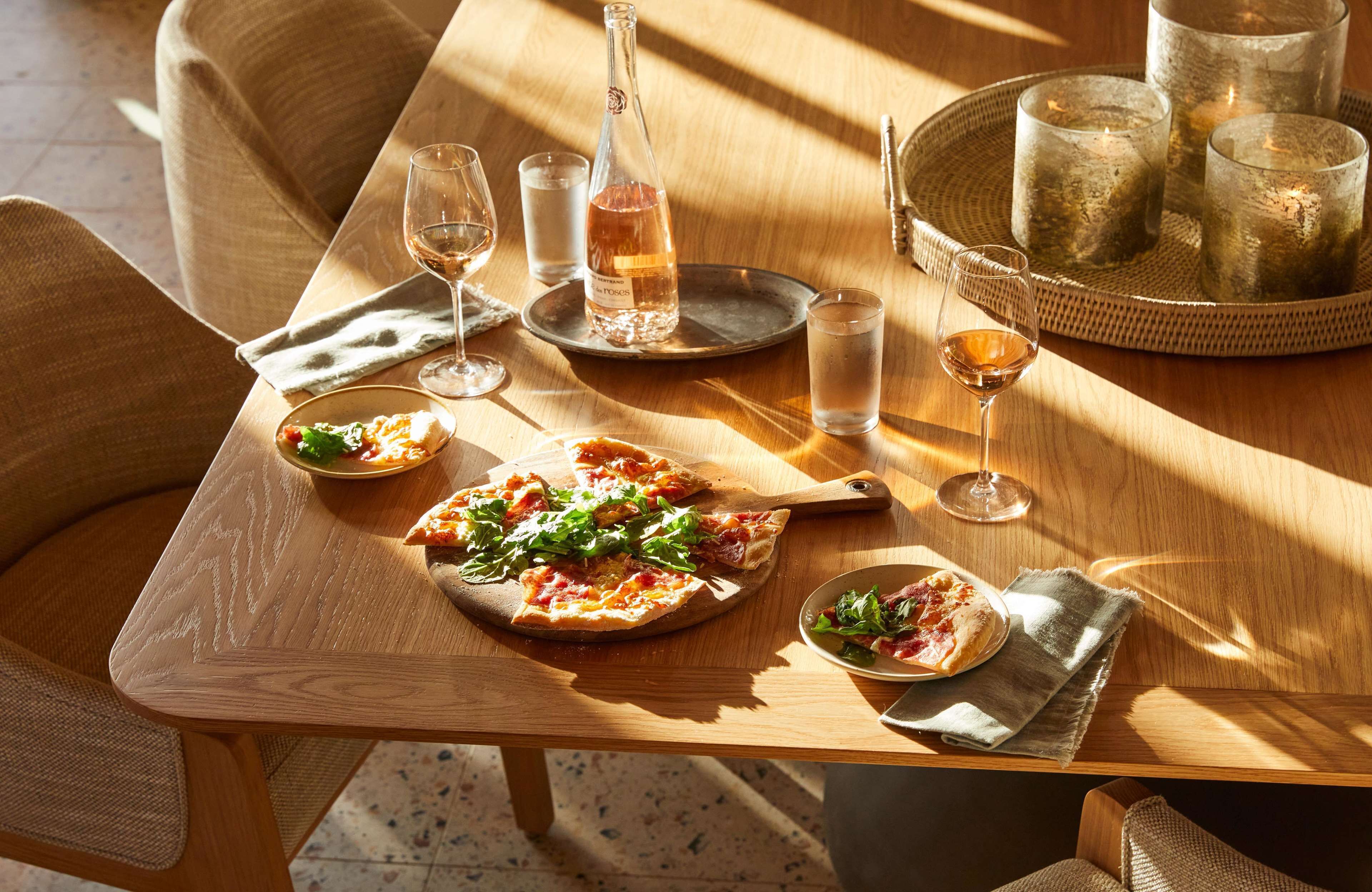 Una mesa de madera con pizza, copas de vino, una botella y velas.