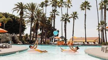 Una piscina con palmeras, sillones de descanso y un jacuzzi.