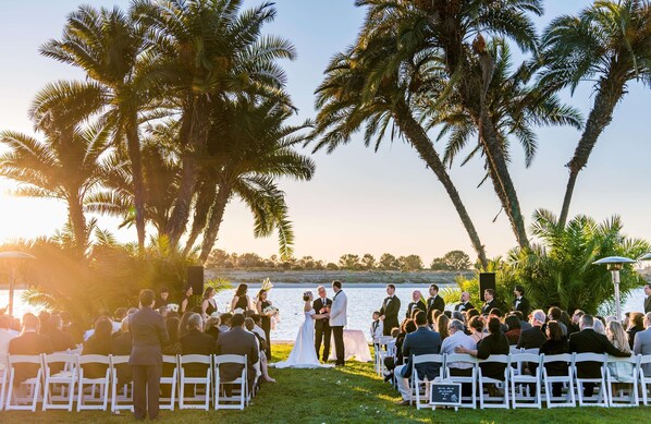 A wedding ceremony outdoors with guests seated on white chairs facing a couple on a grassy area. - San Diego Mission Bay Resort (San Diego)
