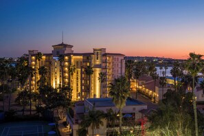 Un hotel de varios pisos con una torre destacada, rodeado de palmeras y vistas del horizonte de la ciudad.