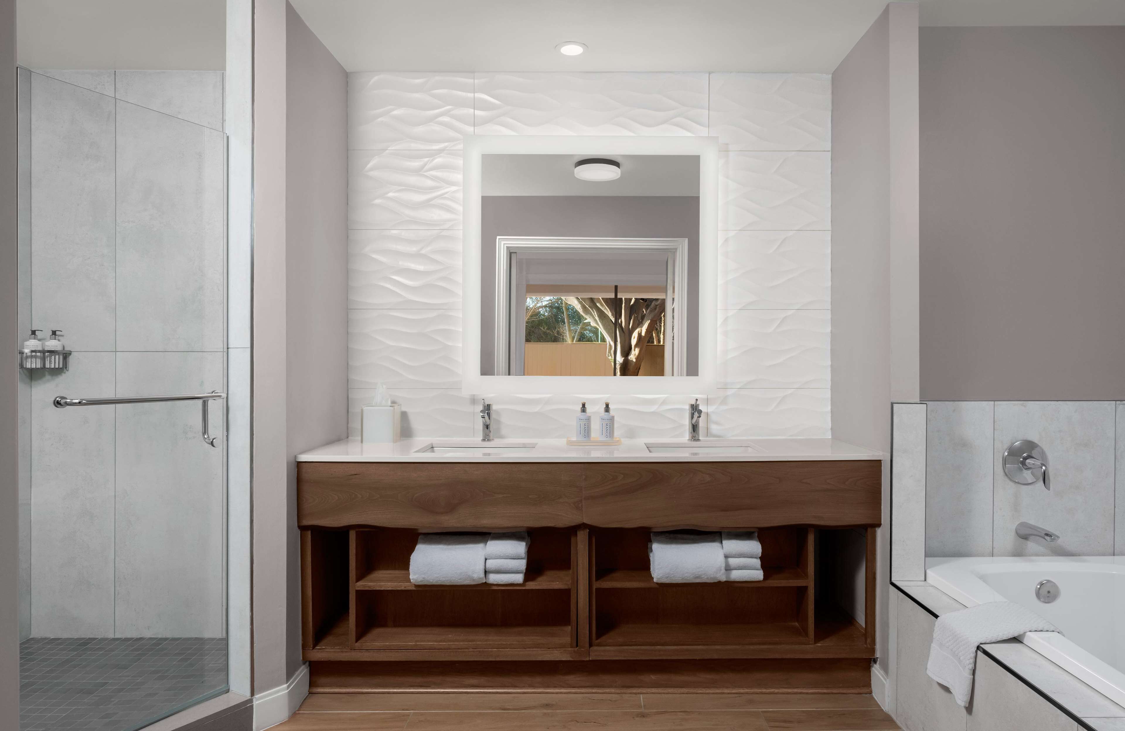 A modern bathroom with a walk-in shower, a double vanity with a wooden base, and a freestanding bathtub.