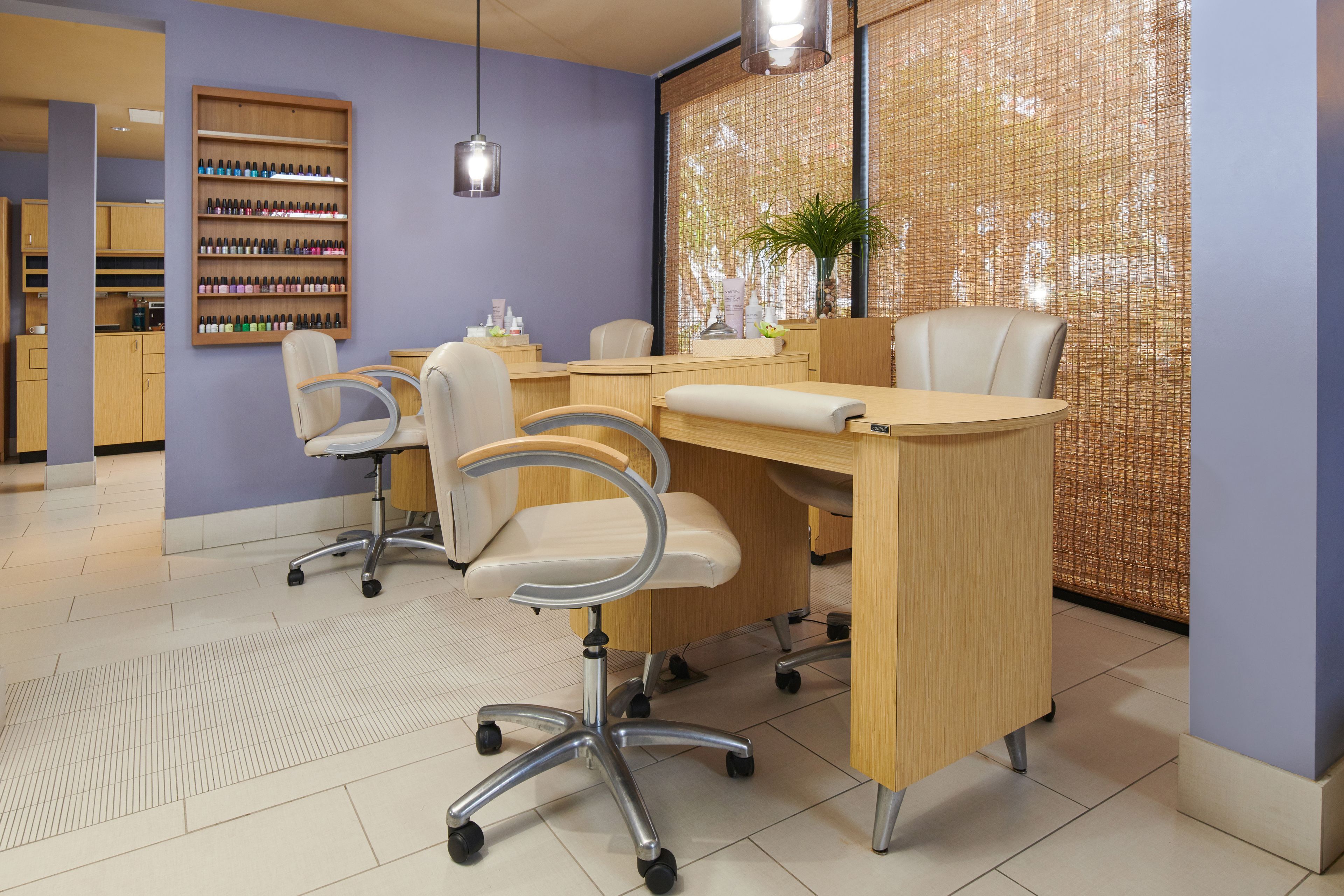 Un salon de manucure moderne, avec un comptoir d’accueil en bois, plusieurs fauteuils et un mur recouvert de vernis à ongles.