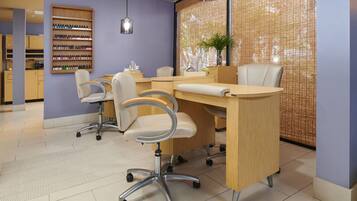 Un salon de manucure moderne, avec un comptoir d’accueil en bois, plusieurs fauteuils et un mur recouvert de vernis à ongles.