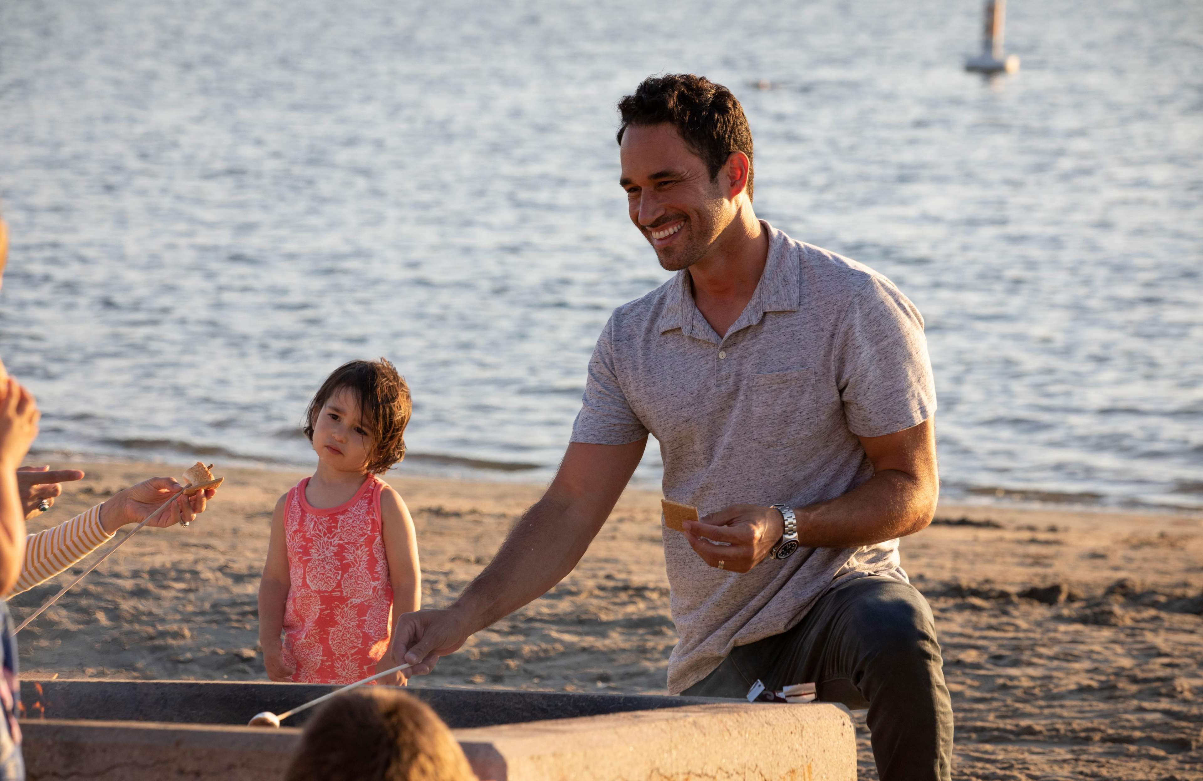 A man and a child on a beach with a body of water in the background.