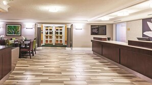 Un vestíbulo de hotel con mostrador de recepción, un comedor con mesas y sillas, y un suelo con estampado tipo espiga.