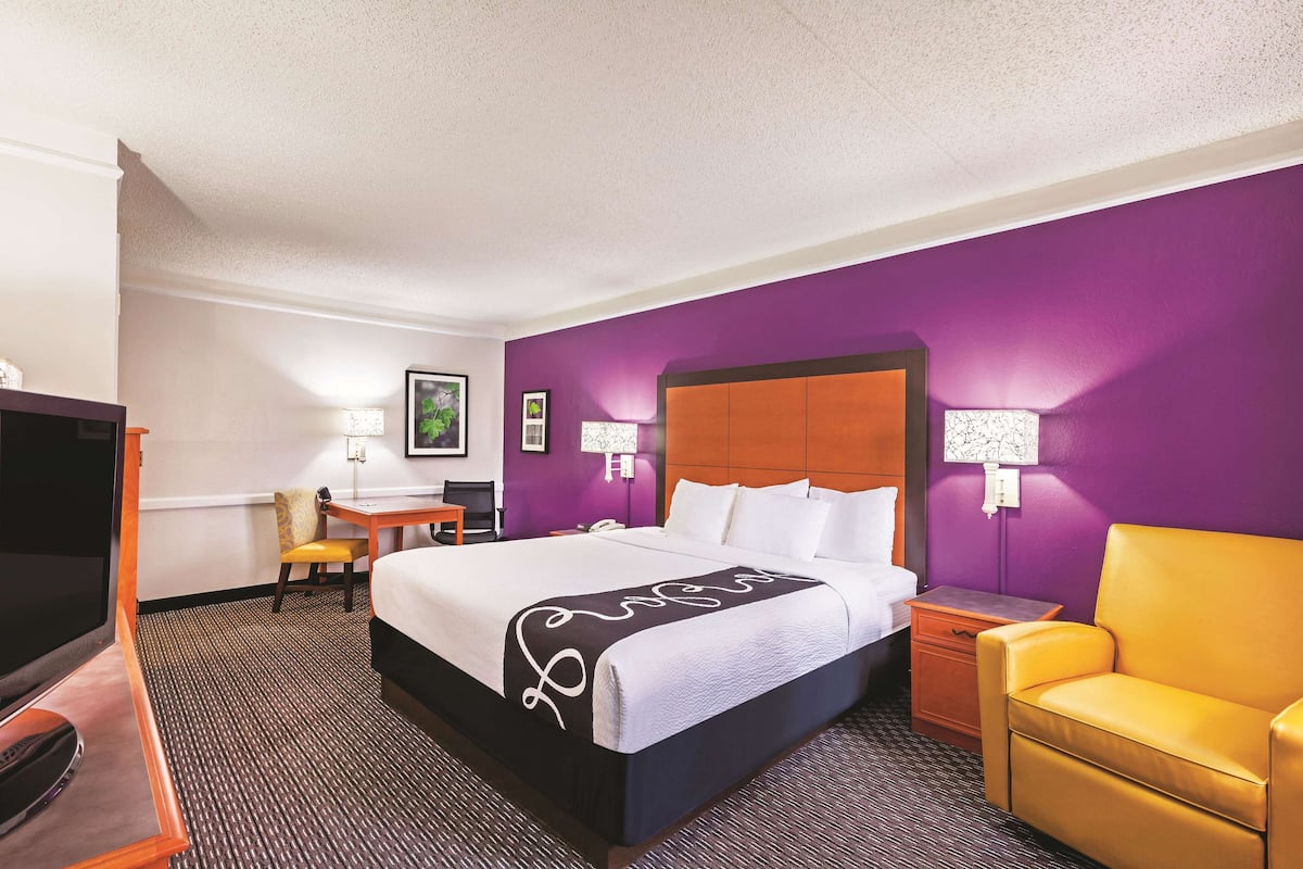 A hotel room with a large bed, a desk, a chair, a TV, and a nightstand.