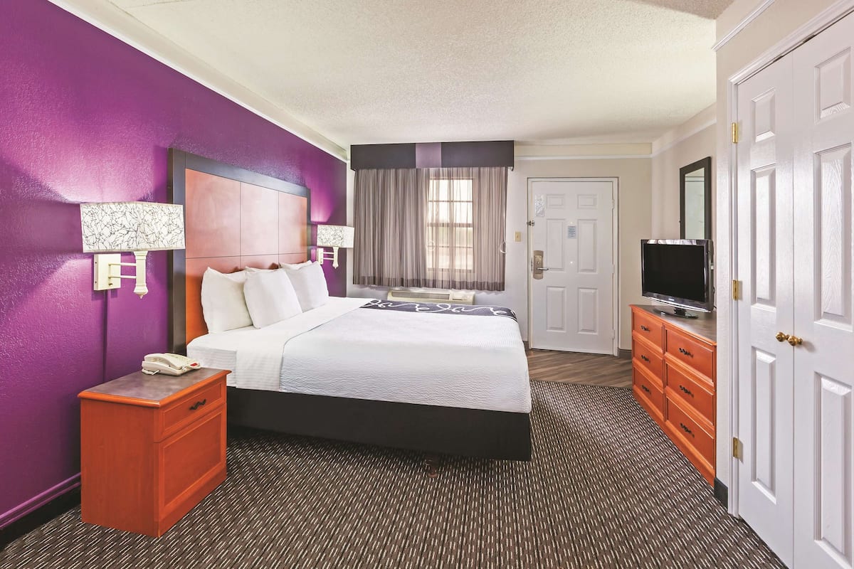 A hotel room with a bed, a nightstand, a dresser, a television, and a door.
