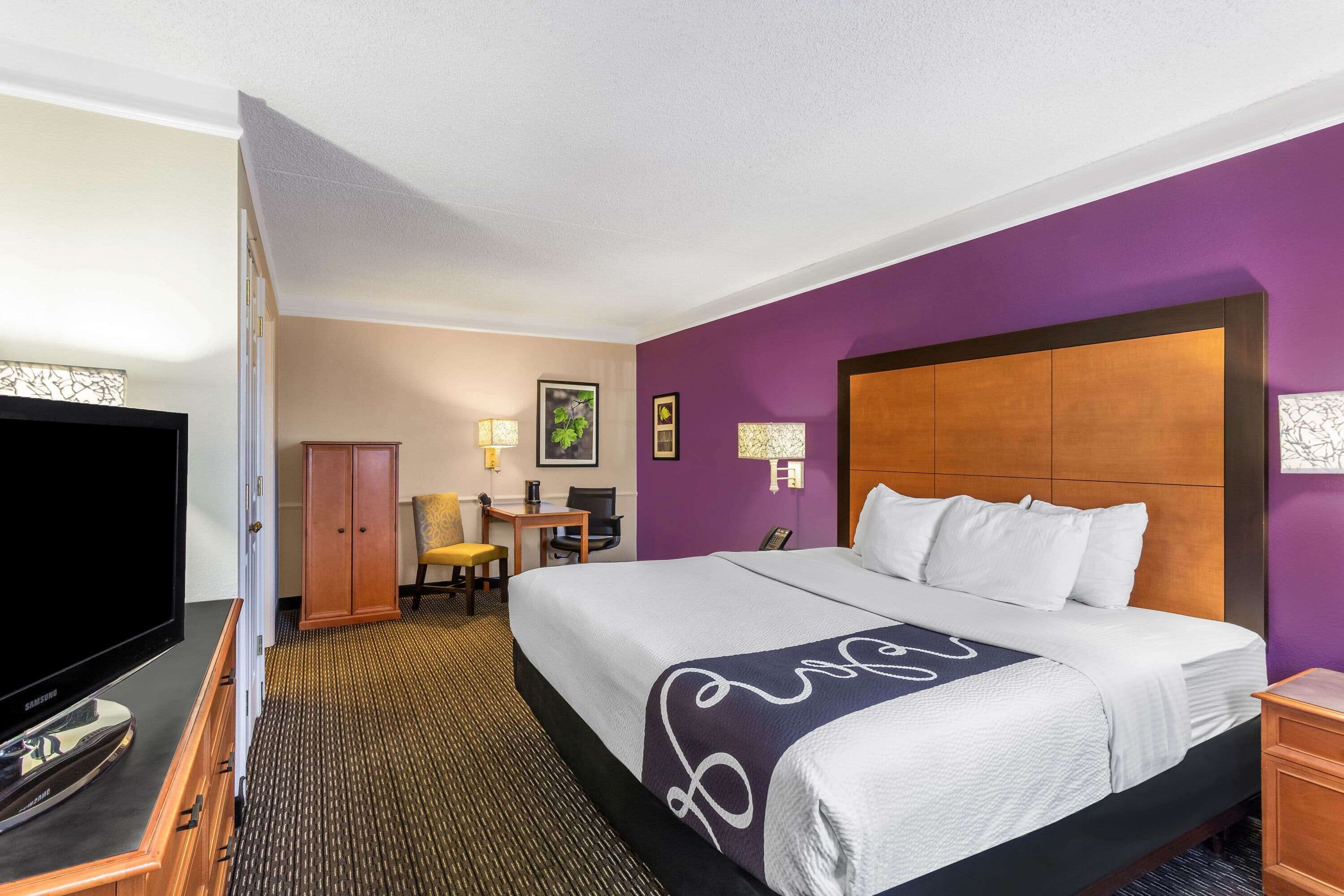 Una habitación de hotel con una cama grande, televisión, escritorio con silla y armario.