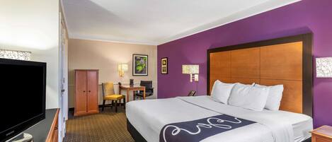 Una habitación de hotel con una cama grande, televisión, escritorio con silla y armario.