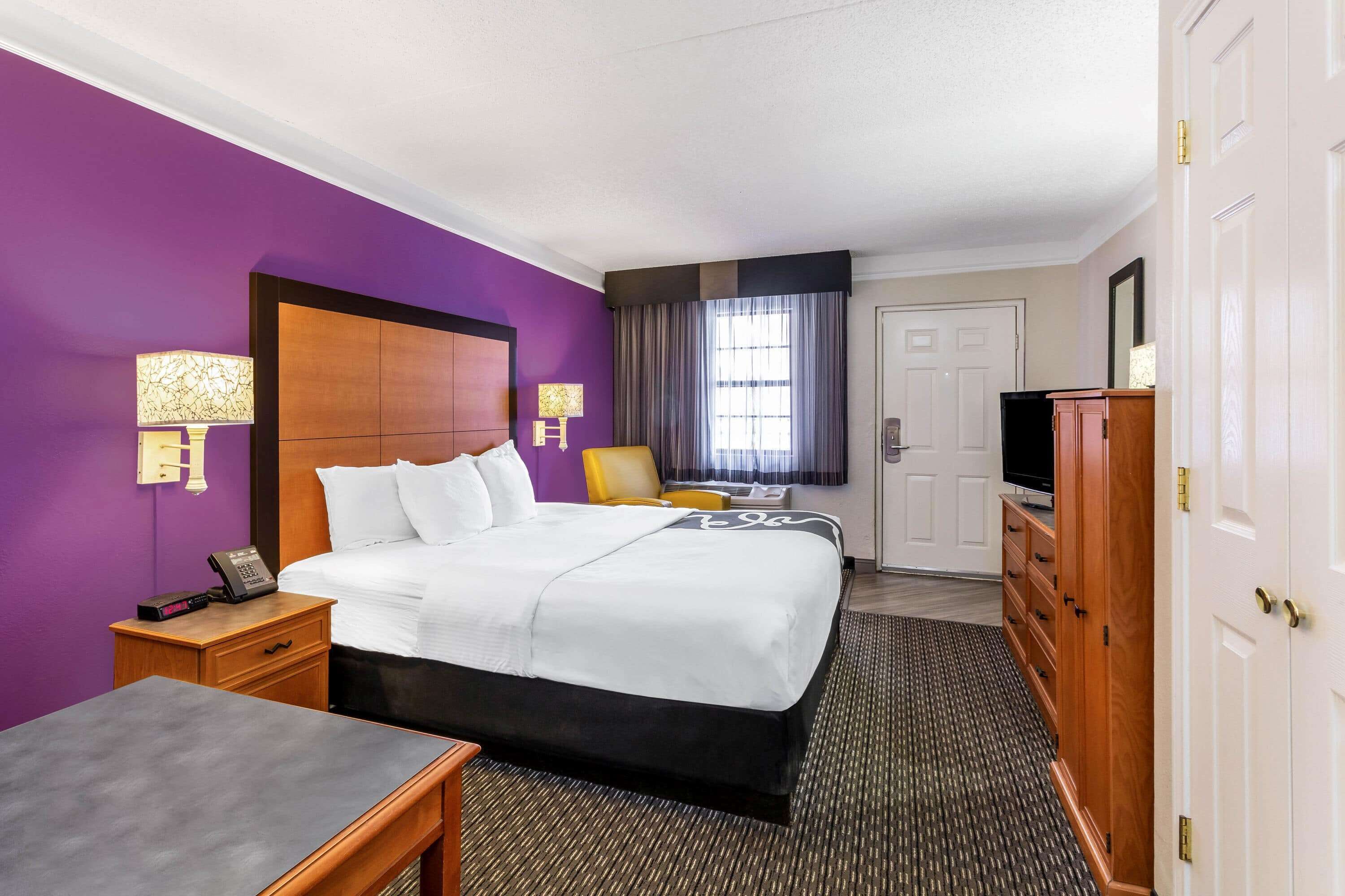 A hotel room with a large bed, a desk, a wardrobe, and a television.