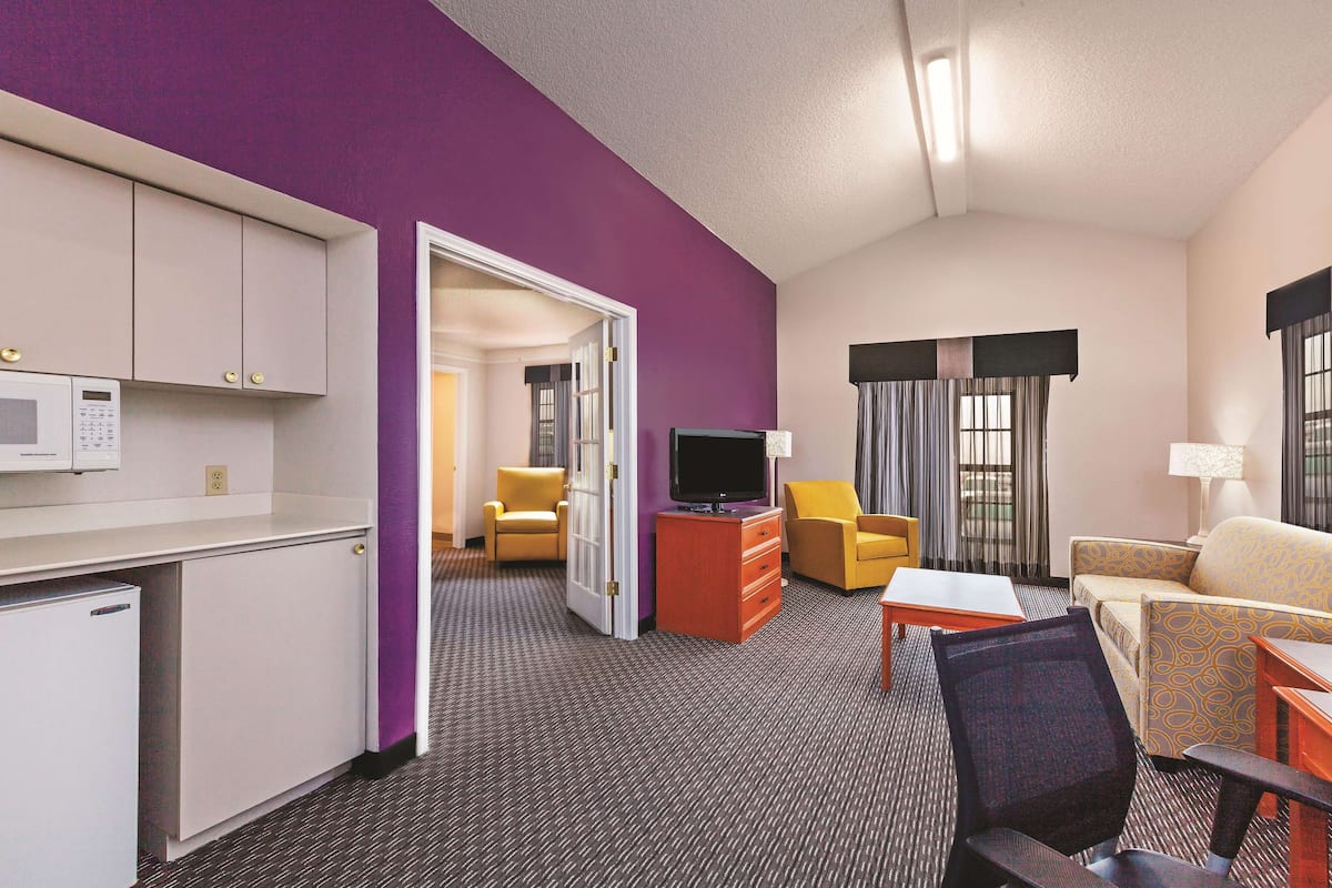 A hotel room with a kitchenette, a TV, a sofa, a chair, and a desk.