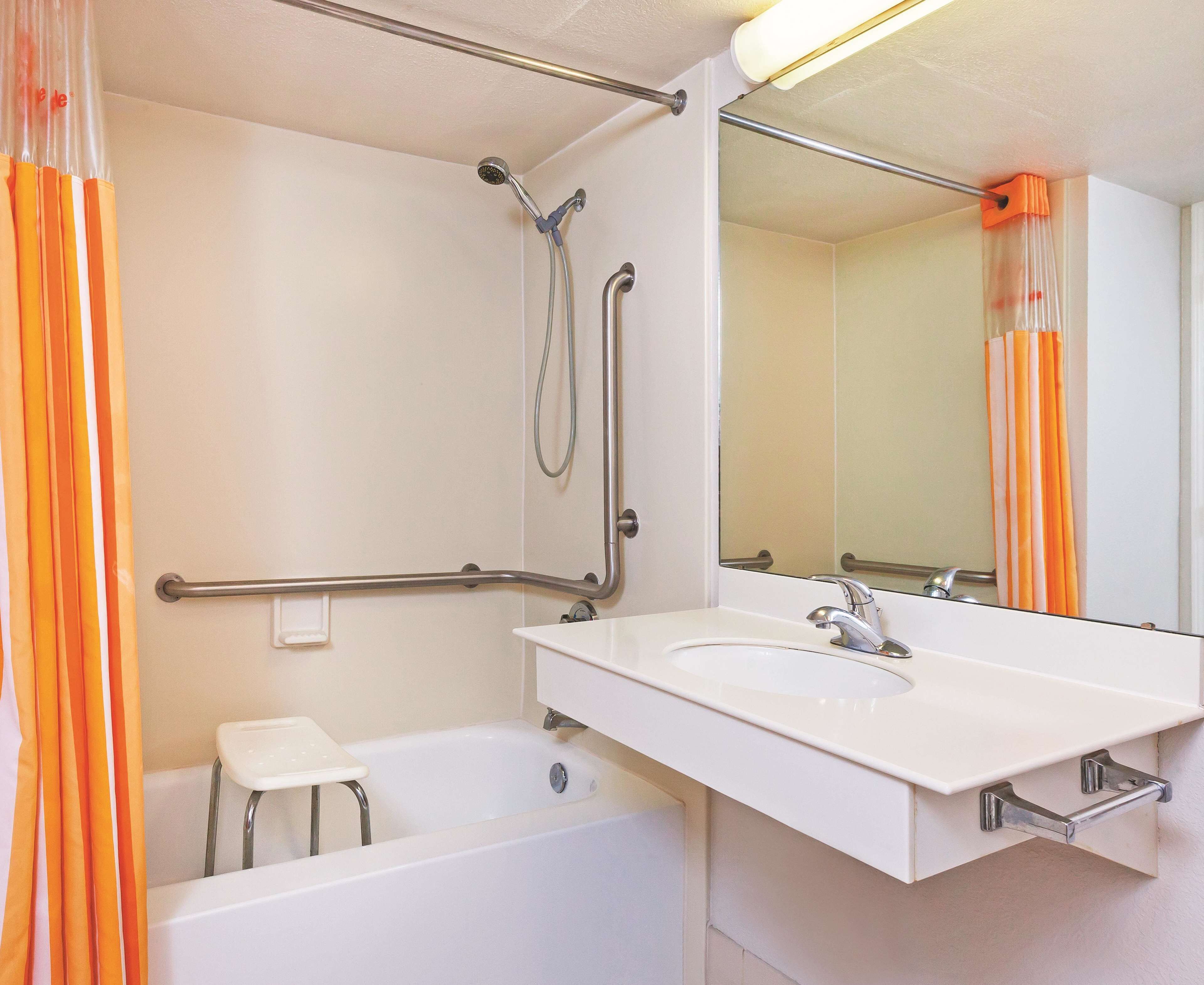 A bathroom with a bathtub, a shower with grab bars, a white sink, and a mirror.