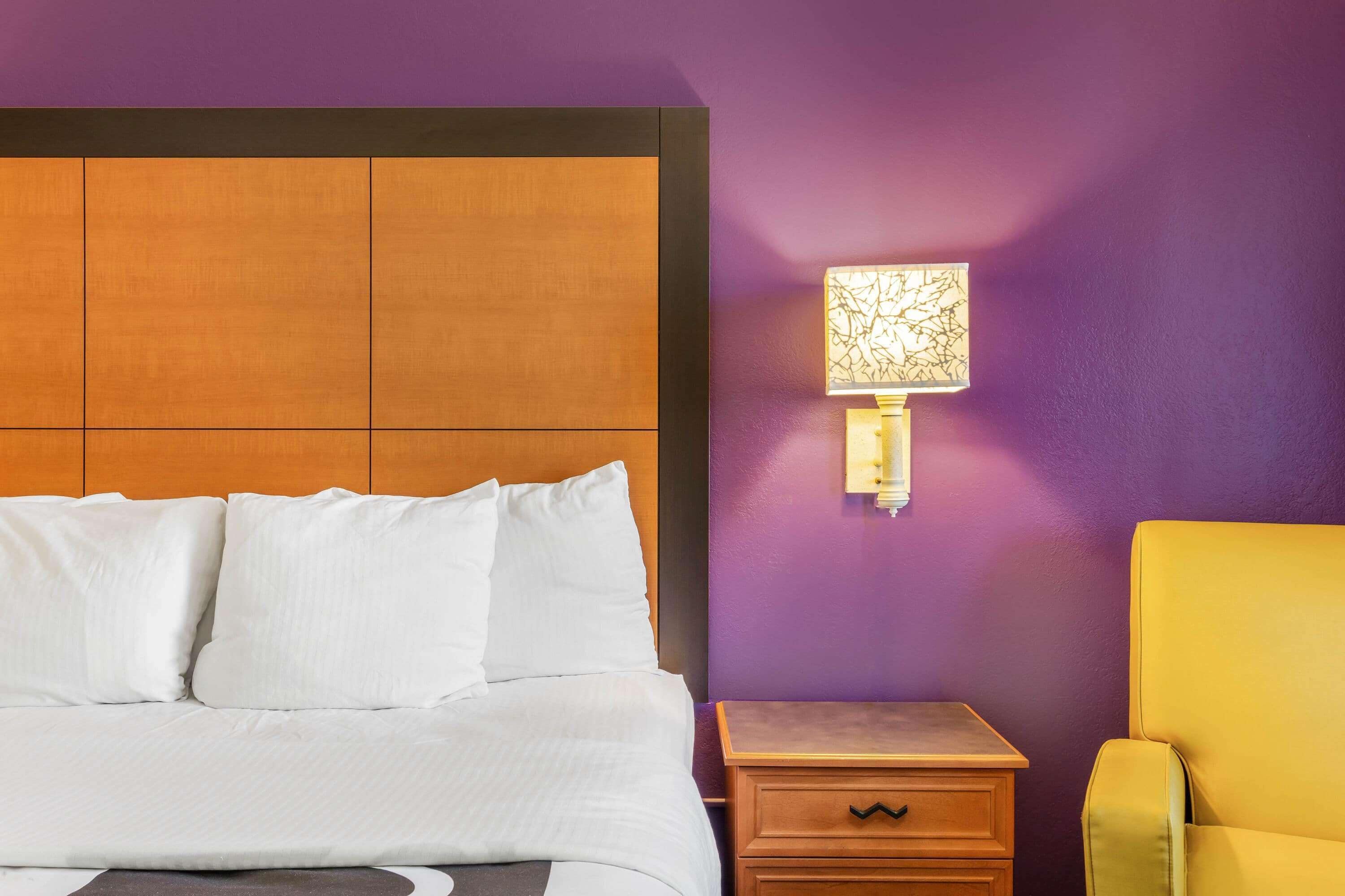 A hotel room with a bed, a nightstand, a lamp, and a yellow armchair.