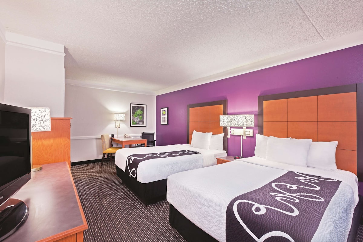 A hotel room with two beds, a desk, a TV, and a chair.