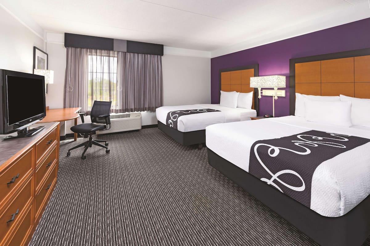 A hotel room with two beds, a desk, a TV, and a window with curtains.