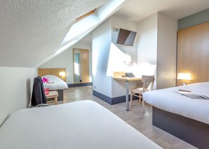 A hotel room with a bed, a desk with a chair, a TV mounted on the wall, and a window providing natural light. - B&B HOTEL Perpignan Nord (Perpignan)