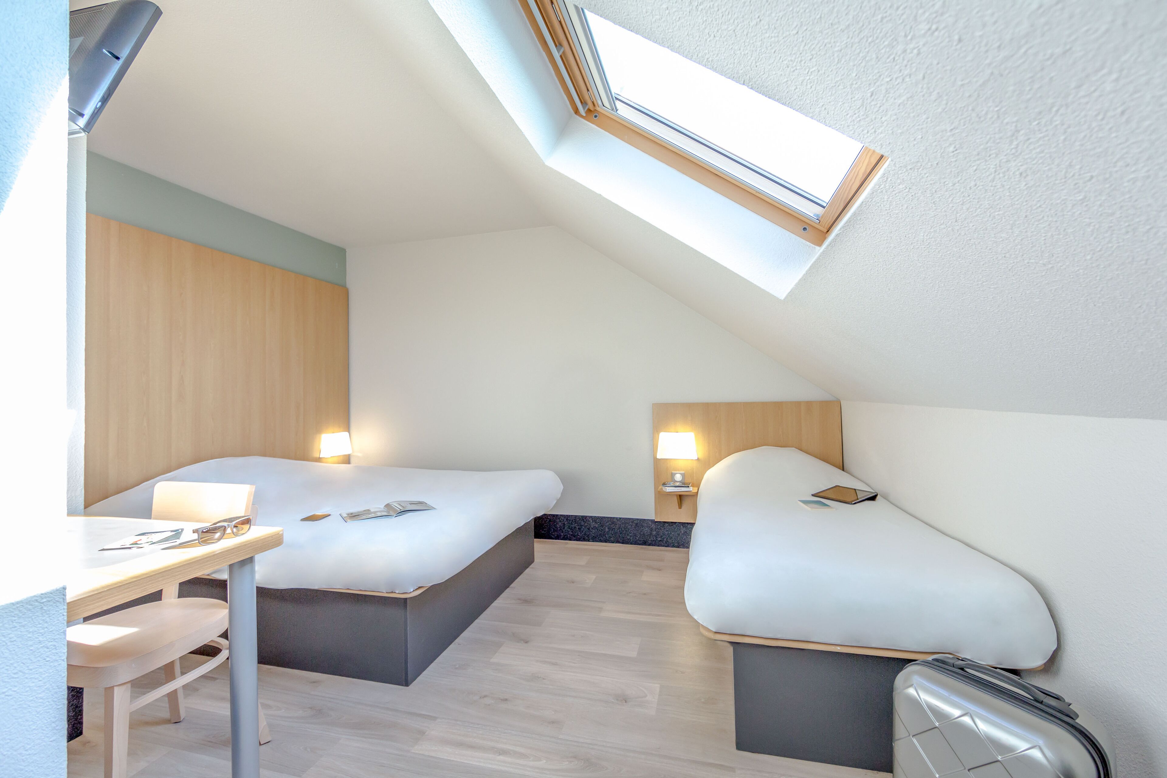 A modern hotel room with two beds, a desk, and a skylight.