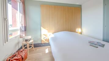 Habitación de hotel con una cama grande, una mesita con una silla, una lámpara y un bolso en el suelo.