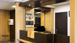 A reception area with a wooden reception desk, a black door, and a poster advertising food. - B&B HOTEL Perpignan Nord (Perpignan)
