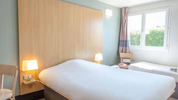 A hotel room with a large bed, bedside lamps, a small table, a chair, and a window with curtains.