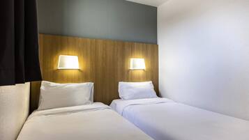 A hotel room with two beds, wooden headboard, and wall-mounted lamps.