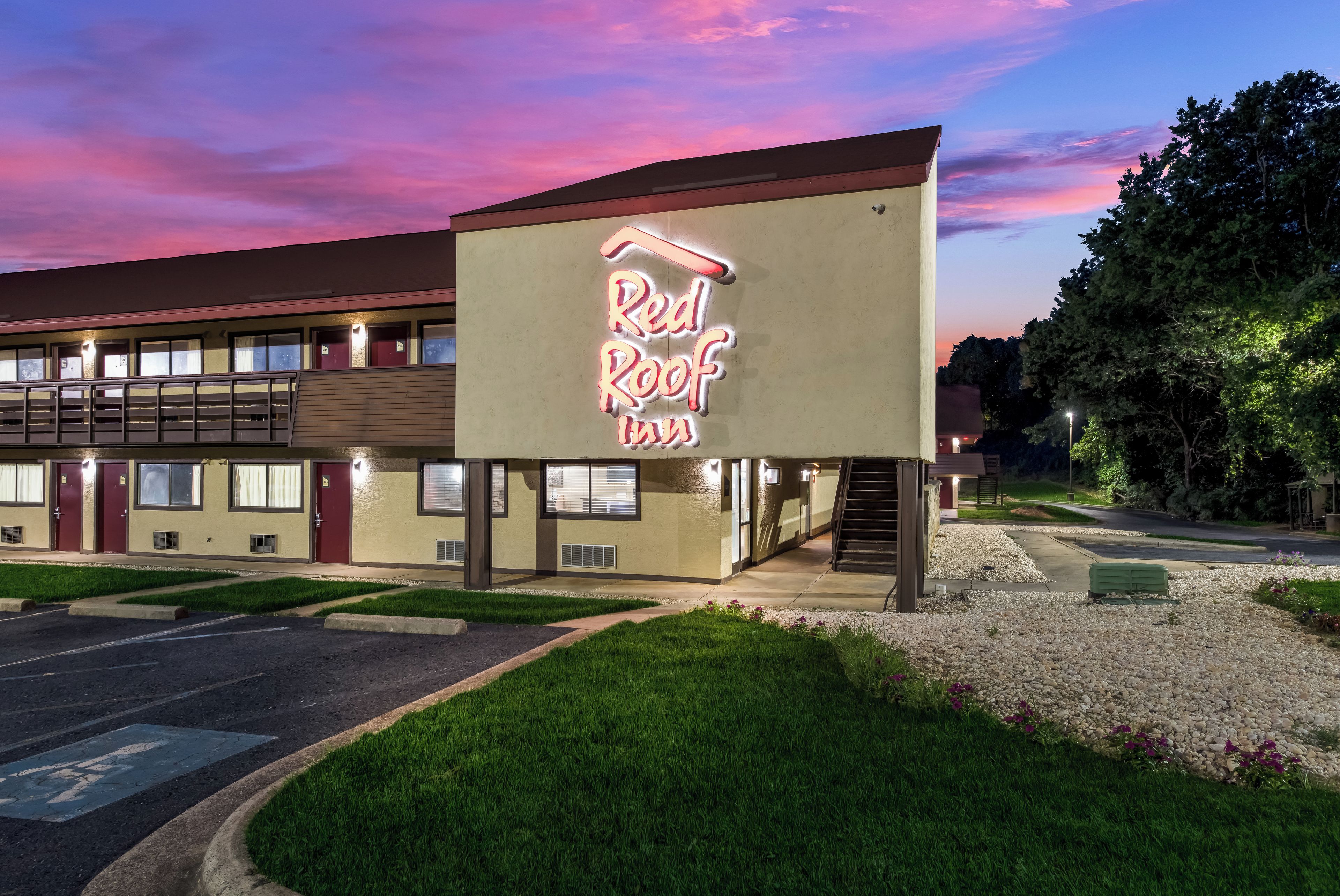 Un motel avec une enseigne au néon indiquant « Red Roof Inn » et un bâtiment à deux étages doté d’une galerie couverte.