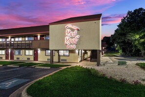 Un motel con un letrero de neón que dice 'Red Roof Inn' y una estructura de dos pisos con un paseo techado.